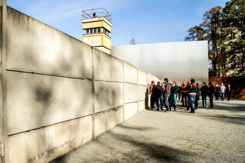 Group standing by a preserved section of the Berlin Wall with a watchtower