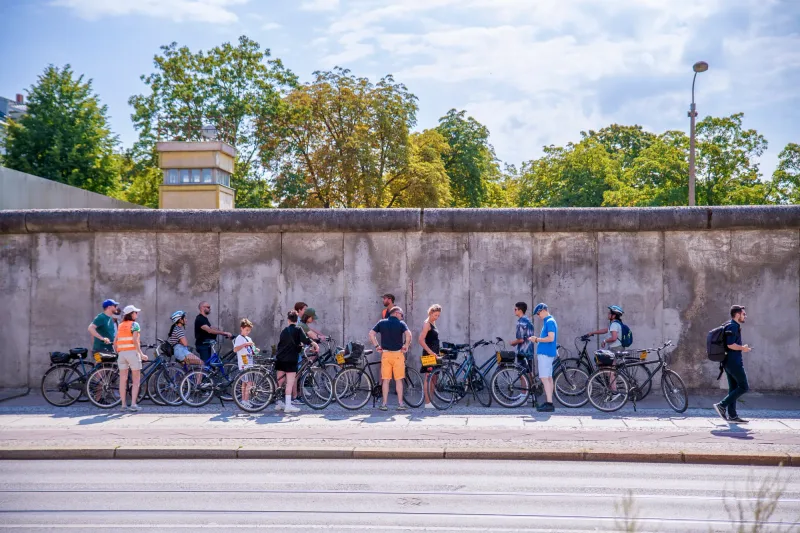 Group of cyclists stopping at a preserved section of the Berlin Wall on a guided bike tour