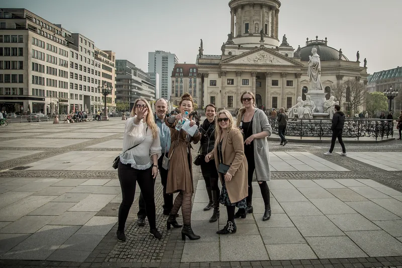 Cheerful team posing on Gendarmenmarkt in front of one of its twin domed cathedrals during a treasure hunt