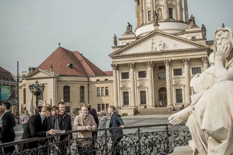 Treasure hunt teams at the railing by the Schiller Monument on Gendarmenmarkt, with one of the twin cathedrals behind